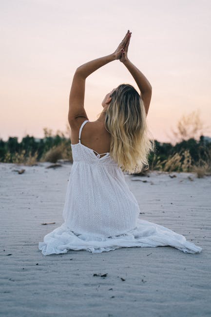 Woman in a white dress meditating on a serene beach during sunset, enhancing calmness and mindfulness.